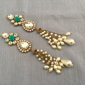 May include: Two ornate, gold-toned hair accessories. Each features a cluster of clear, round and teardrop-shaped crystals, a teal rose, and a large, clear teardrop-shaped crystal. Dangling from each are multiple strands of small, white pearls and larger, pear-shaped pearls.