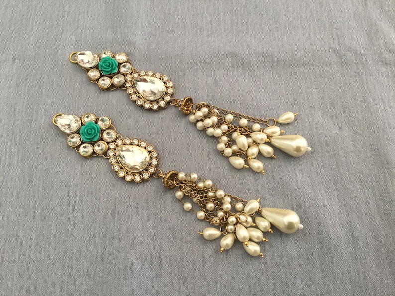 May include: Two ornate, gold-toned hair accessories. Each features a cluster of clear, round and teardrop-shaped crystals, a teal rose, and a large, clear teardrop-shaped crystal. Dangling from each are multiple strands of small, white pearls and larger, pear-shaped pearls.
