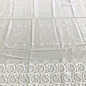 May include: White cotton fabric with a delicate paisley pattern embroidered along the bottom edge. The fabric has a subtle sheen and a soft, lightweight feel.