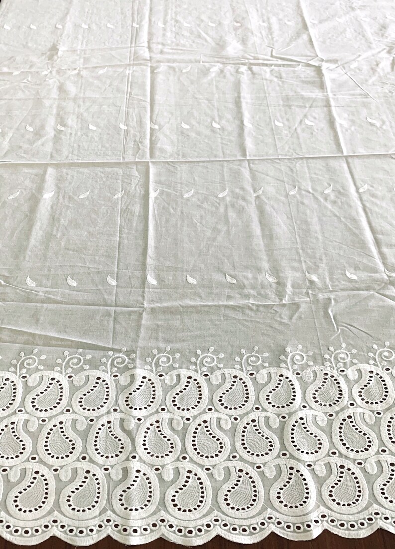 May include: White cotton fabric with a delicate paisley pattern embroidered along the bottom edge. The fabric has a subtle sheen and a soft, lightweight feel.