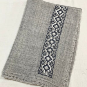 May include: A grey scarf with a decorative border of white sequins and black embroidery.