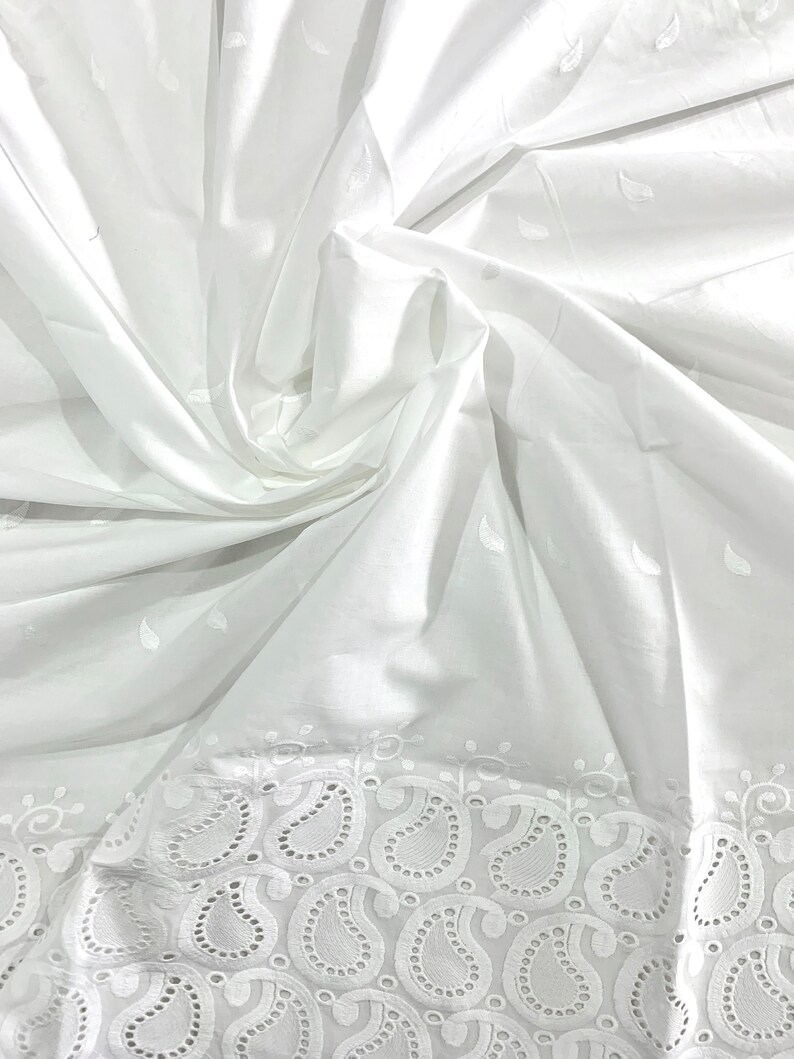 May include: White cotton fabric with a delicate eyelet lace trim featuring a paisley pattern. The fabric is soft and lightweight, perfect for crafting or sewing projects.