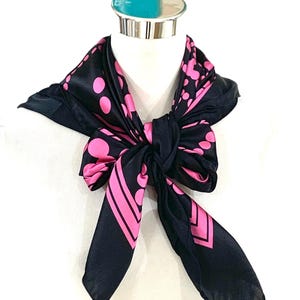 May include: A black silk scarf with a pink polka dot pattern. The scarf is tied in a knot around a mannequin's neck.