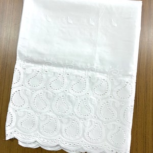 May include: White cotton fabric with a delicate embroidered border featuring a paisley pattern. The border has a scalloped edge.