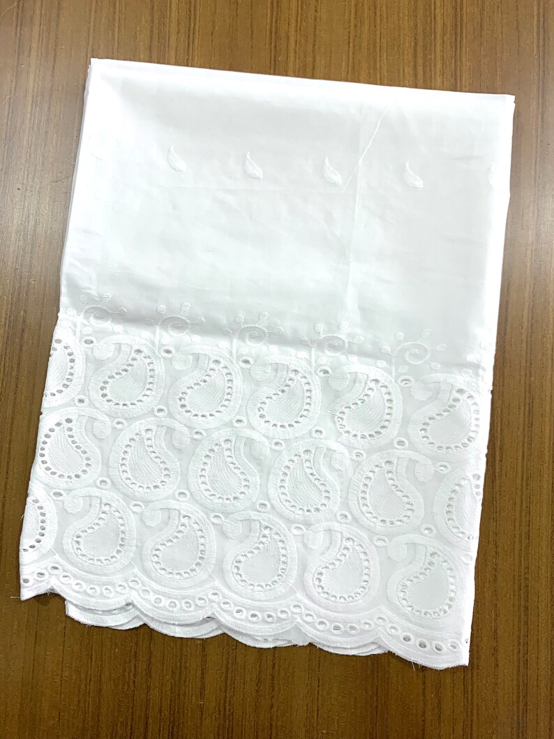 May include: White cotton fabric with a delicate embroidered border featuring a paisley pattern. The border has a scalloped edge.