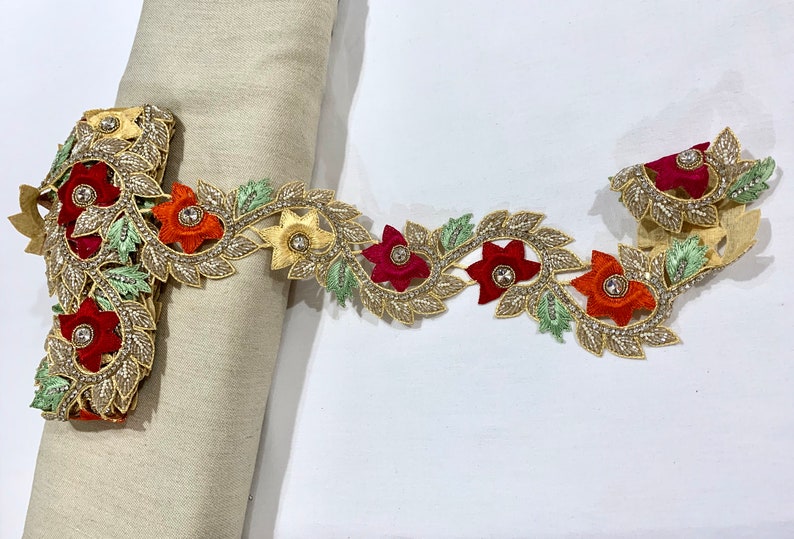 May include: Gold trim lace with red, orange, and green embroidered flowers and leaves. The lace has small clear rhinestones.