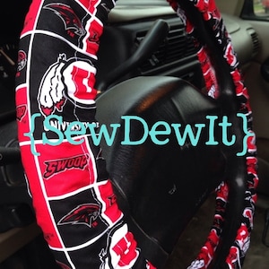 May include: Red and black steering wheel cover with a repeated pattern of a white bird logo and the text "University of" and "Swoop".