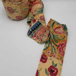 May include: A roll of vintage floral wallpaper with a repeating pattern of red roses, green leaves, and yellow and cream backgrounds. The wallpaper is partially unrolled, revealing the pattern.