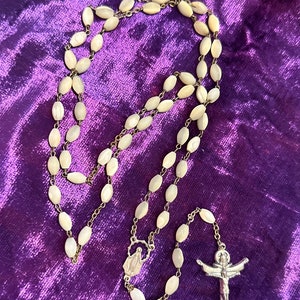 Könnte beinhalten: Eine weiße Perlmuttkette mit einem silbernen Kruzifix und einem silbernen Anhänger der Jungfrau Maria.