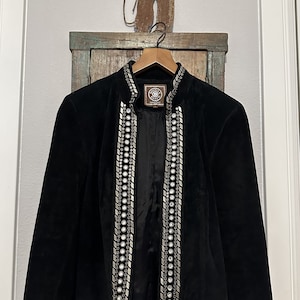 May include: A black suede jacket with silver embellishments and a Double D Ranch label. The jacket has a mandarin collar and long sleeves.