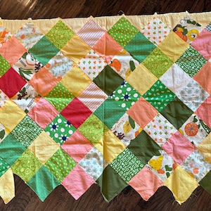 May include: A rectangular patchwork quilt featuring a diamond-patterned arrangement of fabric squares in various colors including yellow, green, pink, red, and white. The quilt includes assorted printed patterns such as flowers, fruits, and dots.