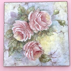 May include: Square artwork featuring a watercolor painting of pink roses with green leaves and buds. The painting has a cracked, aged appearance. The artist's signature, "Mildred Hoffman," is visible in the lower left corner.