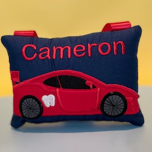 May include: A blue pillow with red embroidered car and the name Cameron. The car has a white tooth on the side.