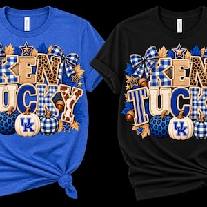 May include: Two short-sleeved t-shirts, one royal blue and one black, each featuring a graphic print that reads KENTUCKY. The design includes blue and white plaid bows, leopard print lettering, autumn leaves, acorns, and three pumpkins with UK logos.
