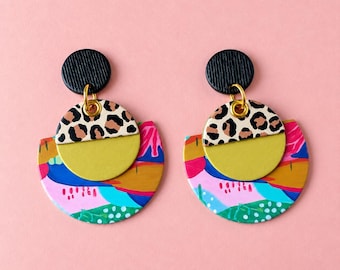 May include: A pair of dangle earrings featuring a black textured stud, a leopard print circle, a solid olive green semi-circle, and a larger semi-circular base with a multi-colored abstract pattern in blue, pink, yellow, and green.
