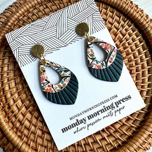 May include: Teardrop-shaped earrings with a floral pattern and dark teal textured bottom. The earrings have a gold-colored stud and are displayed on a white card with a black and white geometric design. The card reads "monday morning press where passion meets paper."