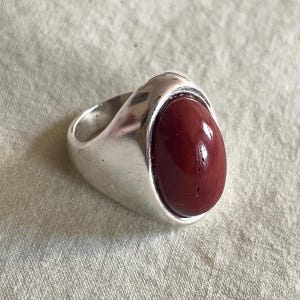 May include: A silver ring with a large, oval-shaped, dark red gemstone.