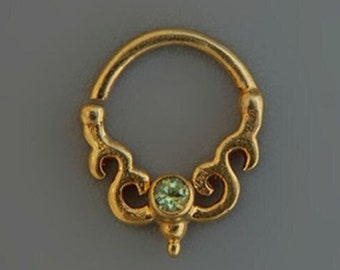 May include: Gold septum ring with a green gemstone in the center and intricate scrollwork design.