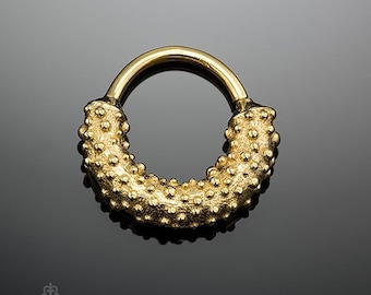May include: Gold hoop earring with a textured surface. The earring is a simple circle with a raised, bumpy texture.
