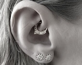 Könnte beinhalten: Nahaufnahme eines Ohrs mit einem silbernen Creolenohrring im Helix-Piercing und zwei silbernen sternförmigen Ohrringen in den Ohrläppchen-Piercings.