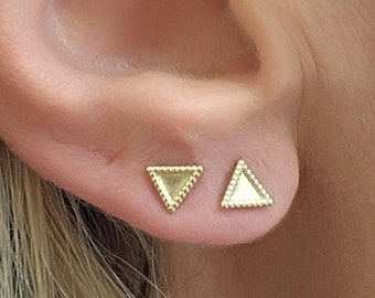 Könnte beinhalten: Ein Paar goldene Dreiecks-Ohrstecker mit strukturiertem Rand. Die Ohrringe sind klein und zart.