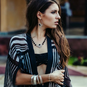 May include: A woman wearing a black and white striped kimono with a black bandeau top. She is wearing silver jewelry, including a necklace with a black stone pendant and earrings with black stone accents.