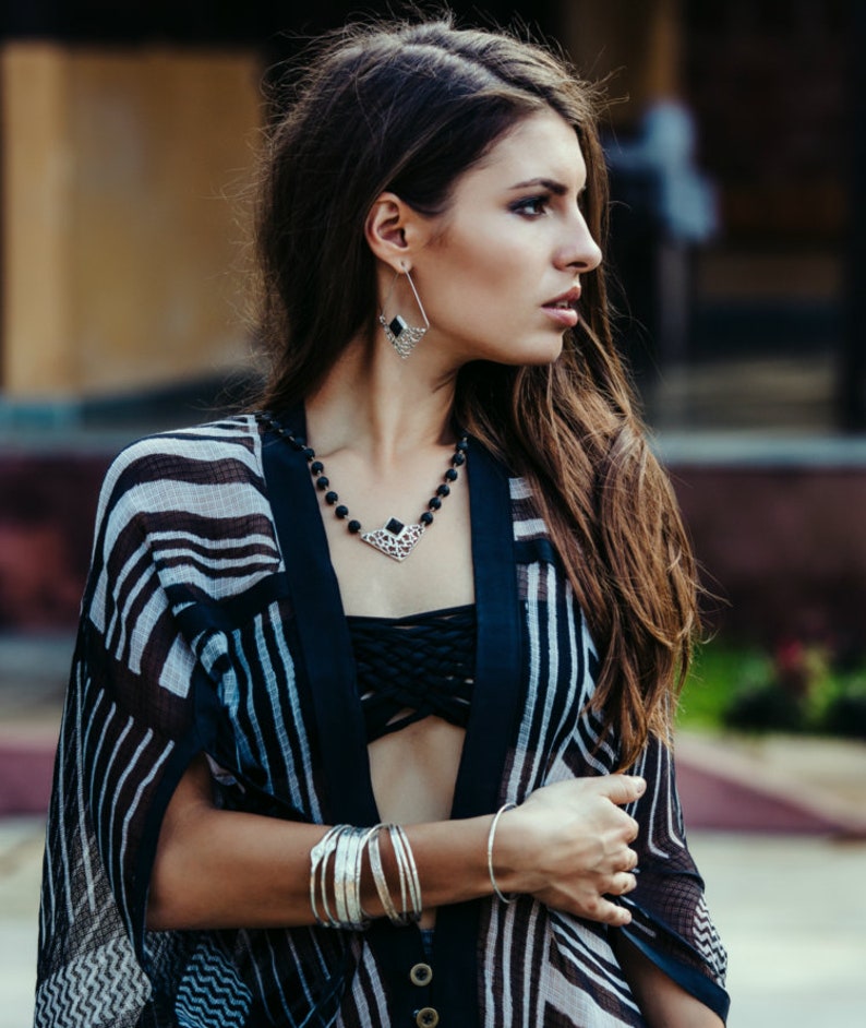 May include: A woman wearing a black and white striped kimono with a black bandeau top. She is wearing silver jewelry, including a necklace with a black stone pendant and earrings with black stone accents.