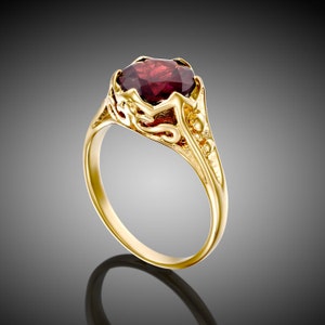 May include: A gold ring with an ornate design and a large, dark red gemstone.