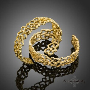 May include: Two gold rings with a delicate, intricate design resembling a floral pattern. The rings are stacked on top of each other, creating a layered effect.