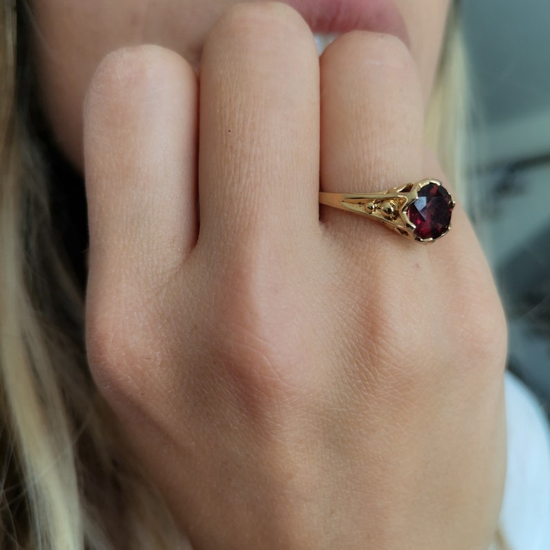 May include: A gold ring with a red gemstone set in a delicate, ornate design.