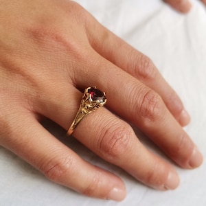 May include: A gold ring with a red gemstone set in a detailed floral design.