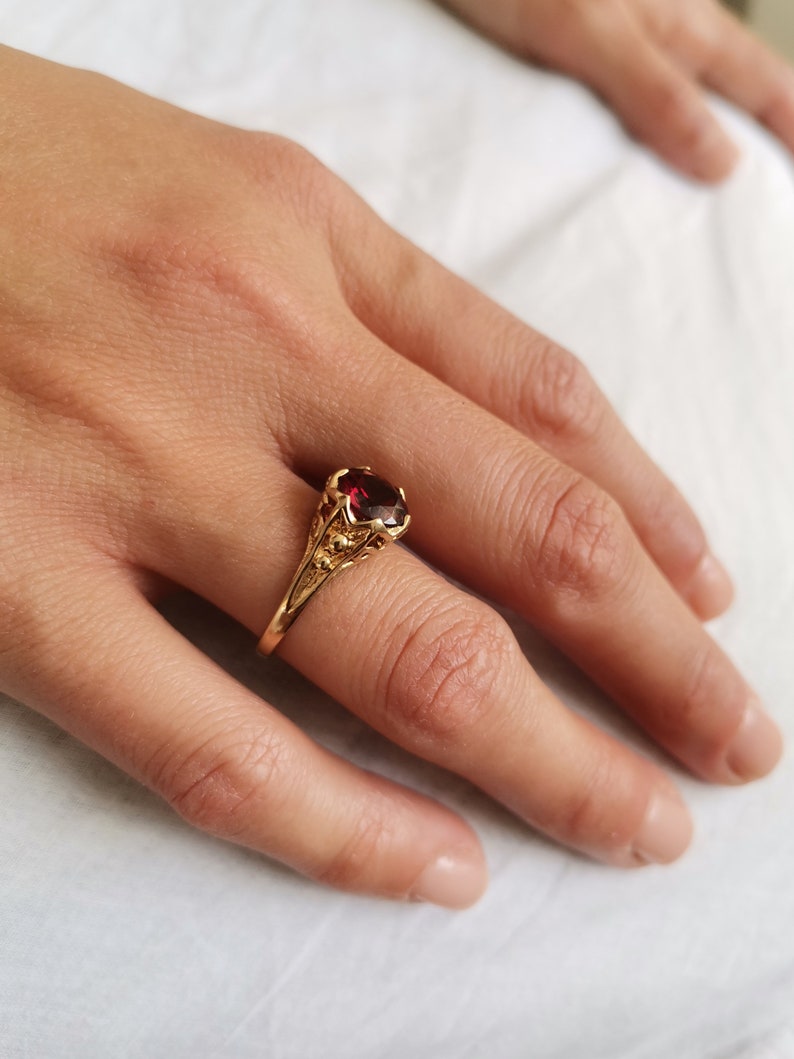 May include: A gold ring with a red gemstone set in a detailed floral design.