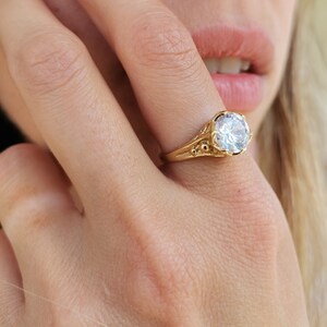 May include: A gold ring with a large, clear, round gemstone. The ring has a detailed, ornate design.