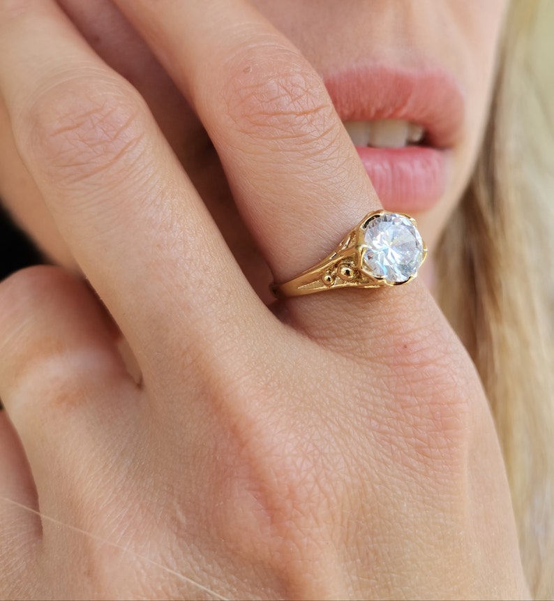 May include: A gold ring with a large, clear, round gemstone. The ring has a detailed, ornate design.