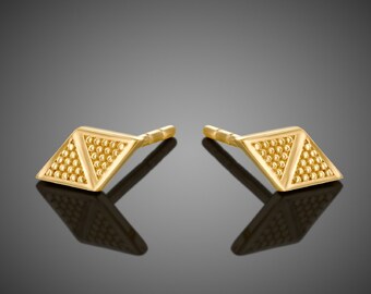 May include: A pair of gold-toned stud earrings with a geometric pyramid design. The earrings are made of small, textured beads.