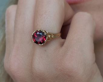 May include: A gold ring with a large, red gemstone set in a decorative, ornate setting.