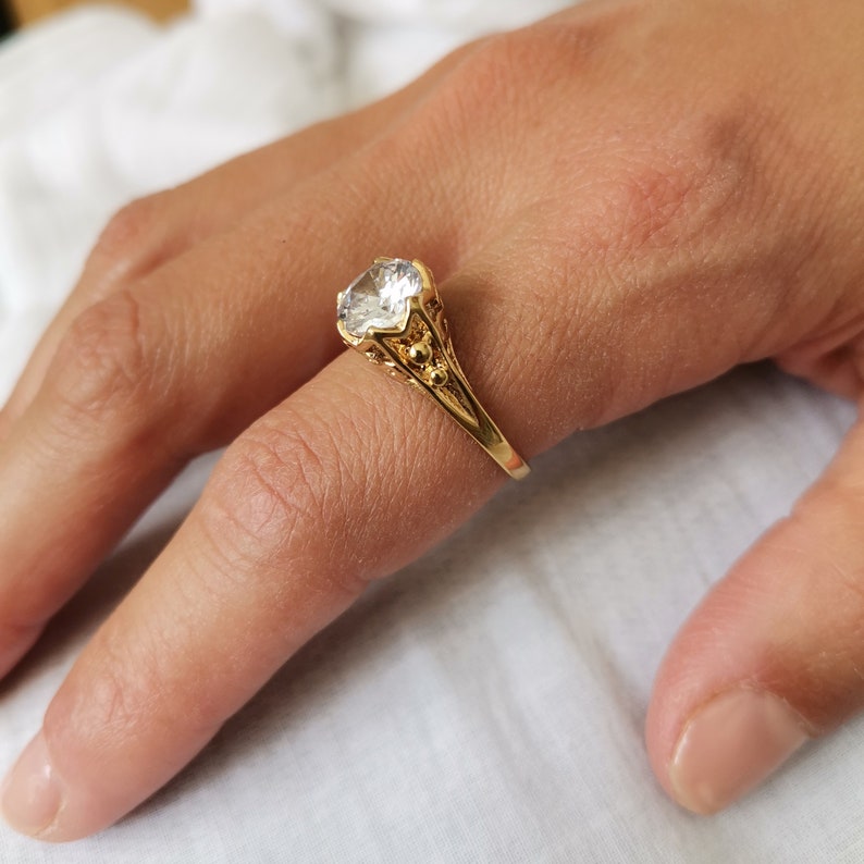 May include: A gold ring with a large, clear, round gemstone. The ring has a detailed, ornate design.