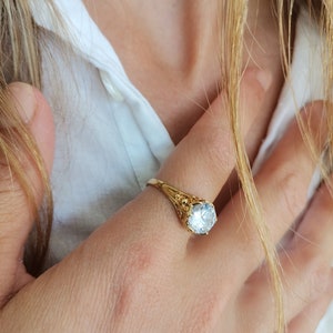 May include: A gold ring with a large, clear, round gemstone. The ring has a delicate, ornate design.