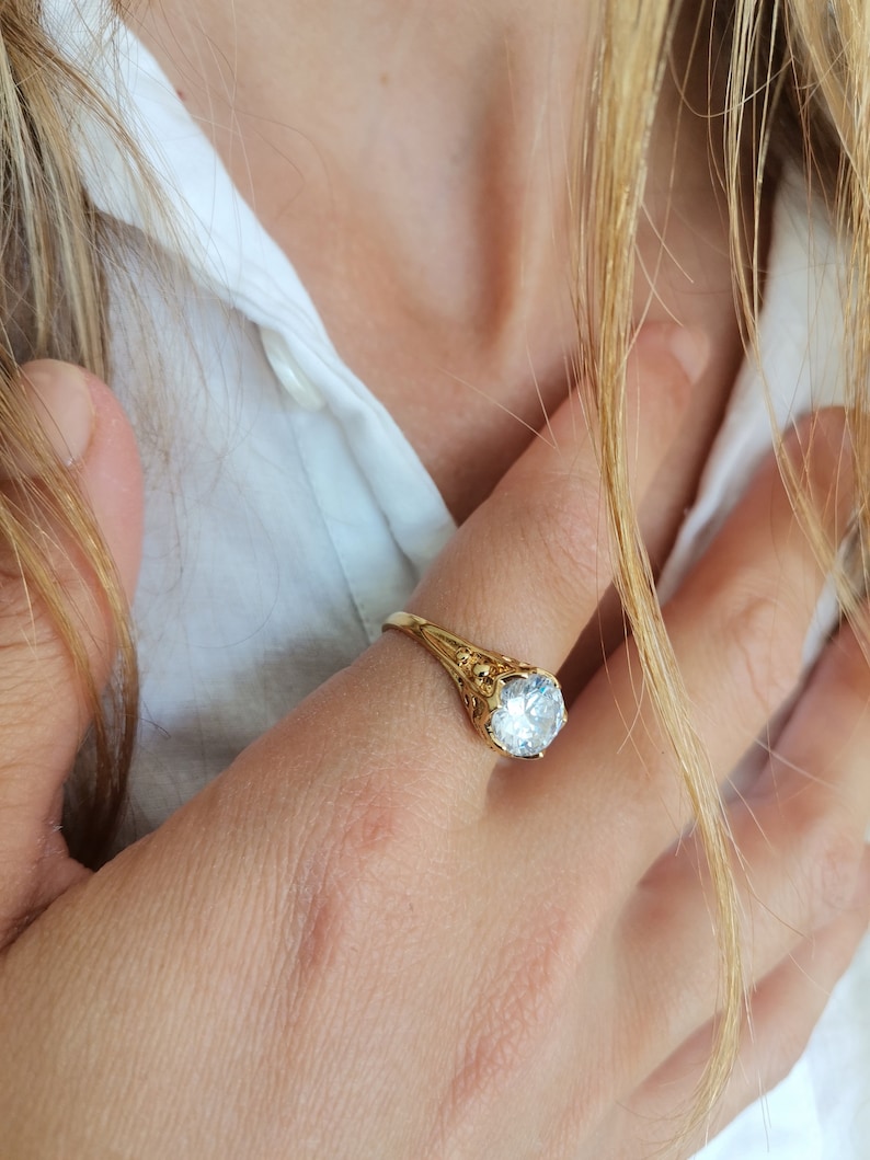 May include: A gold ring with a large, clear, round gemstone. The ring has a delicate, ornate design.