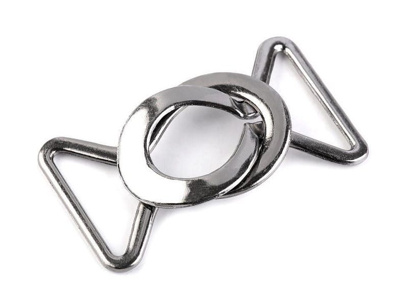May include: Silver metal buckle with a D-ring and two triangular loops. The buckle is designed for attaching straps or belts.