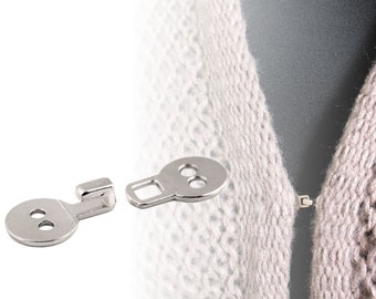 May include: Two silver metal sweater clips with a hook and a round button. The clips are used to fasten a sweater or cardigan.