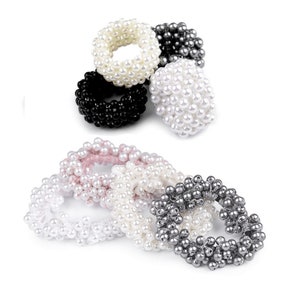 Può includere: Set di sei elastici per capelli in perle di vari colori, tra cui bianco, nero, rosa e grigio. Gli elastici per capelli sono realizzati con piccole perle rotonde che sono infilate insieme per formare un cerchio.