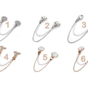 May include: Six pairs of decorative shawl clips with double chains. Each clip features a different design with rhinestones, pearls, and a choice of silver or gold finishes. The clips are numbered 1 through 6.