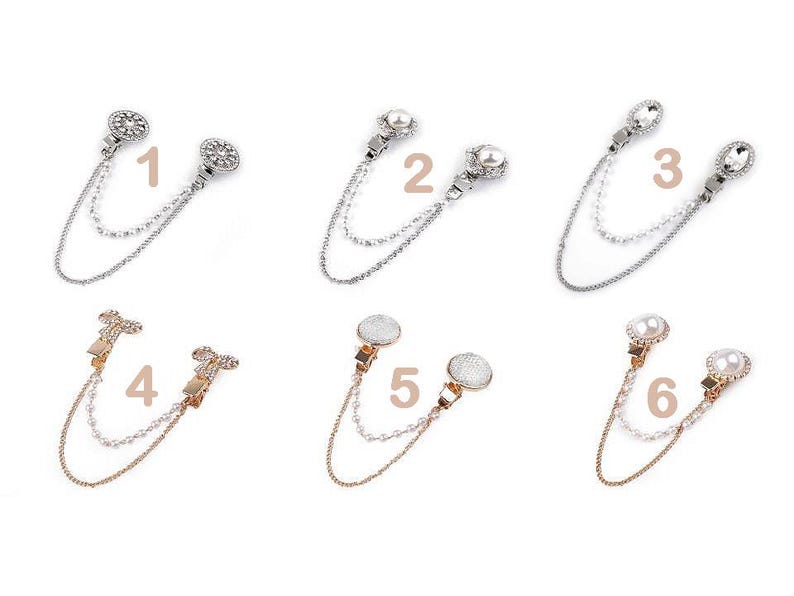 May include: Six pairs of decorative shawl clips with double chains. Each clip features a different design with rhinestones, pearls, and a choice of silver or gold finishes. The clips are numbered 1 through 6.