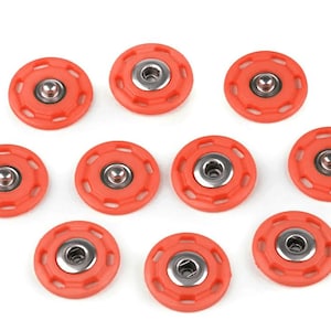Peut inclure: Dix boutons-pression orange avec un centre en métal argenté sont disposés sur fond blanc. Chaque bouton-pression a un design circulaire avec plusieurs trous sur le bord.