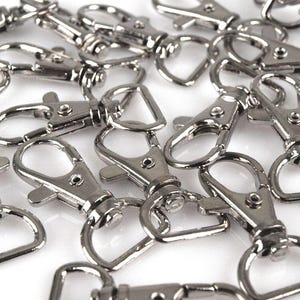 May include: A pile of silver-toned metal keychains with a swivel clasp. The keychains are all the same size and shape, and they are arranged in a random pattern.