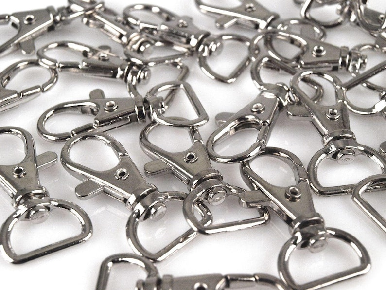May include: A pile of silver-toned metal keychains with a swivel clasp. The keychains are all the same size and shape, and they are arranged in a random pattern.
