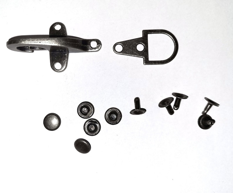 May include: A set of silver-toned metal hardware for leather crafting. The set includes a hook and loop closure, a D-ring, and several rivets.
