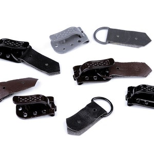 Pode incluir: Conjunto de fechos metálicos pretos, castanhos e cinzentos com correias de couro. Os fechos têm um design texturizado e são usados para prender.