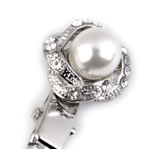 May include: A silver hair clip with a pearl and crystal embellishment. The pearl is white and the crystals are clear.